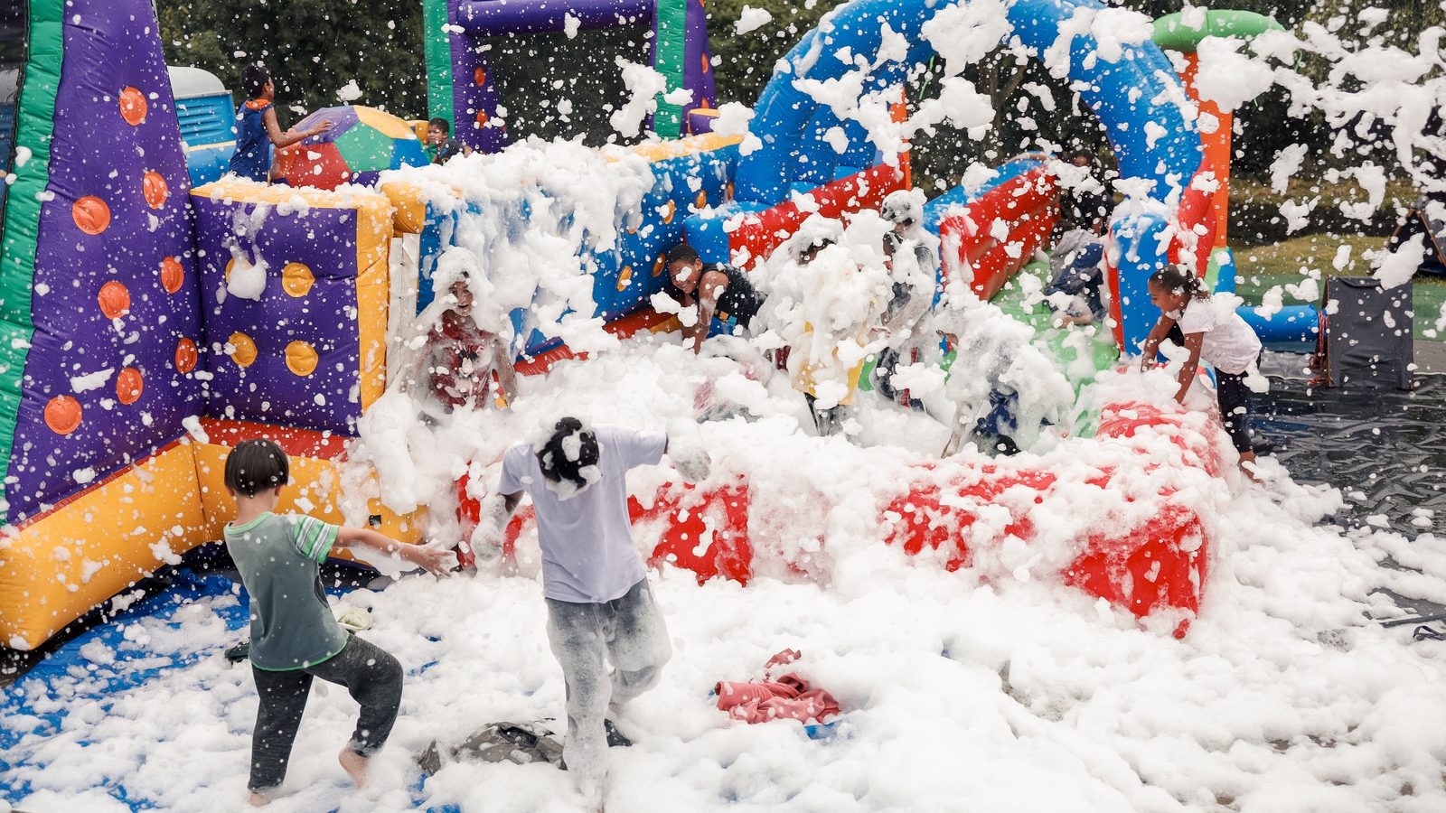 Crianças brincando na festa da espuma ao lado dos infláveis
